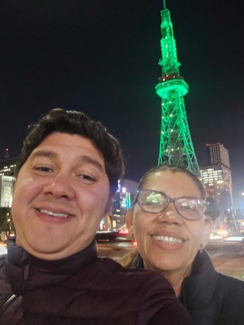 Andrés y su mamá de noche, con la torre de Nagoya iluminada de verde detrás.